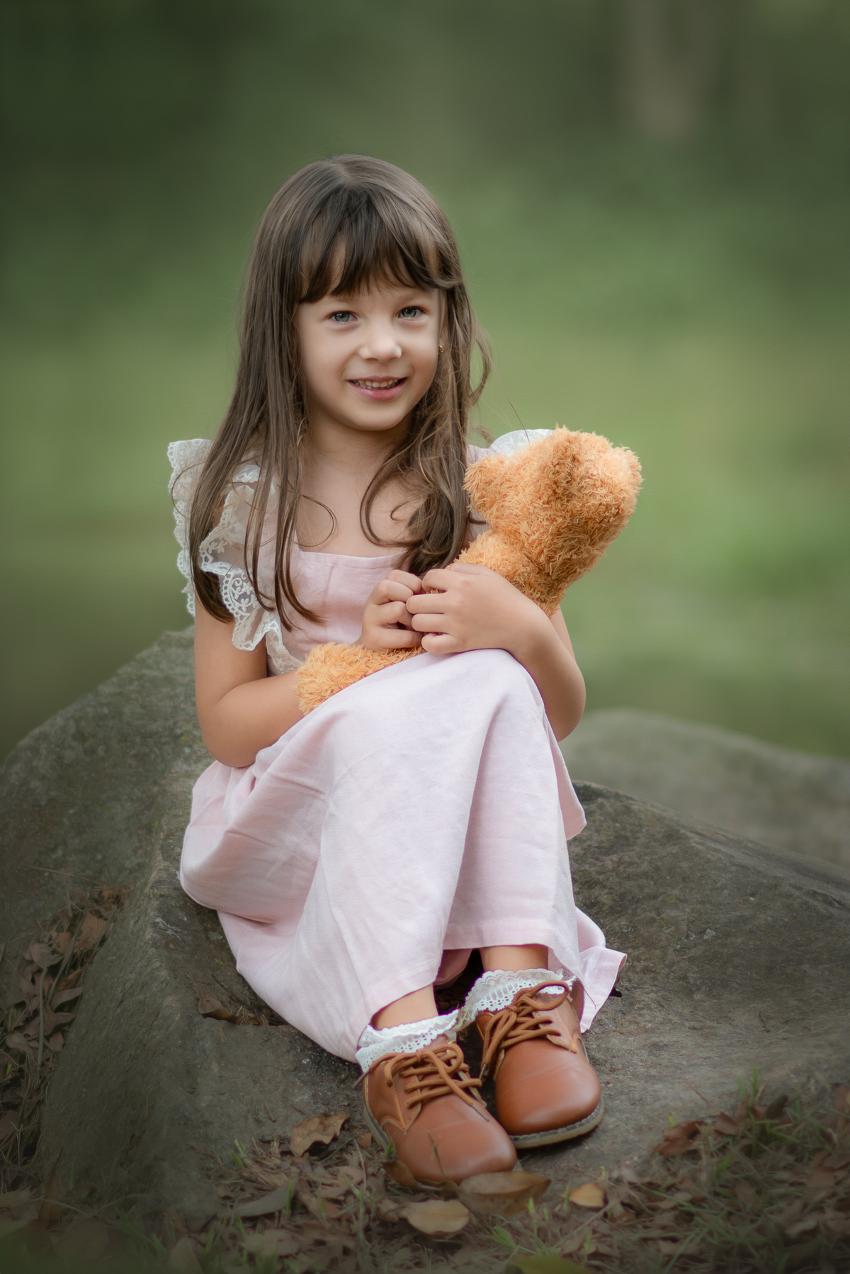 Uma crianças usando um vestido rosa bem estilo camponesa e brincando com um ursinho de pelúcia marrom, em um parque, durante seu ensaio artistico.