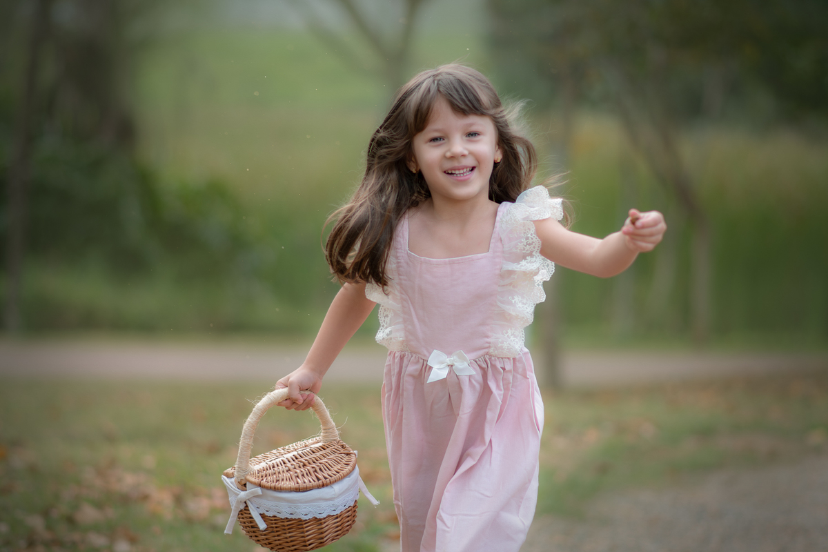 Uma crianças usando um vestido rosa, estilo camponesa e brincando em um parque com folhas, durante seu ensaio artistico.
