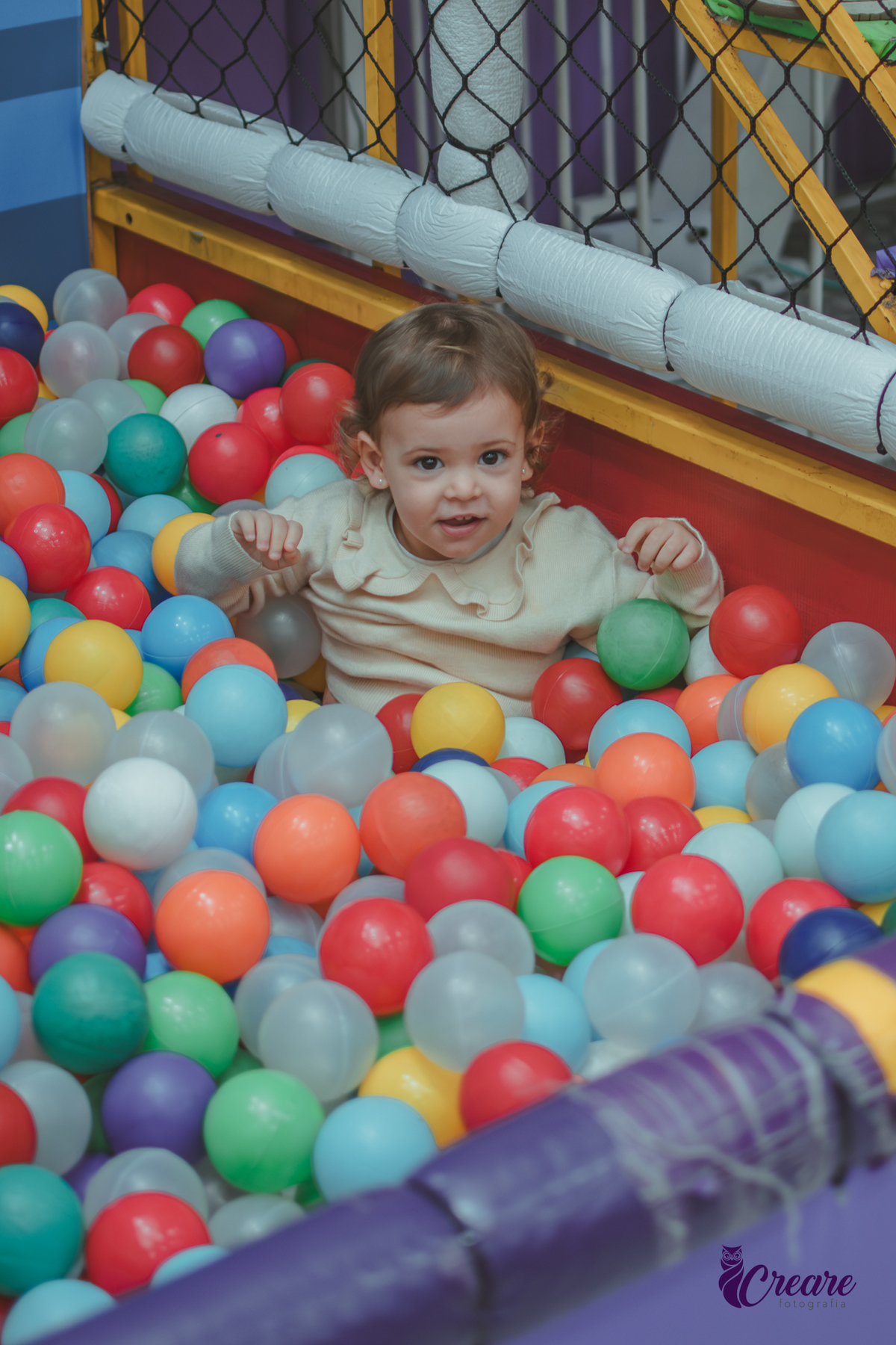 Uma menina de dois anos dentro de uma piscina de bolinhas em seu aniversário no Buffet Happy House.