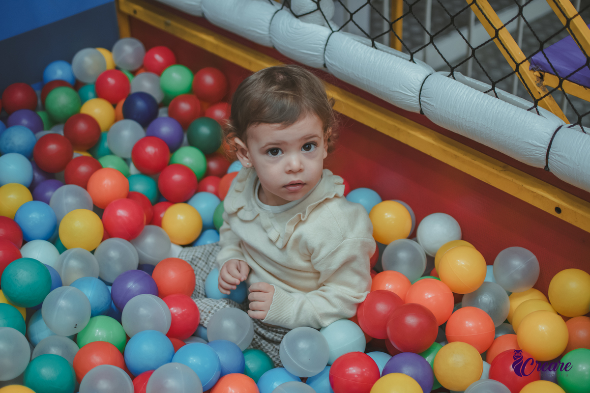 Uma menina de dois anos dentro de uma piscina de bolinhas em seu aniversário no Buffet Happy House.