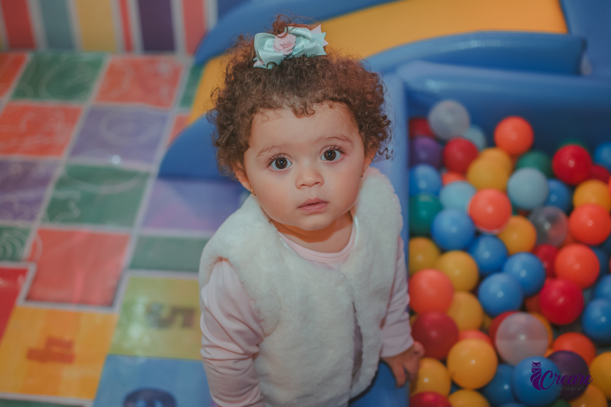 Uma criança olhando para cima, em frente uma piscina de bolinhas durante festa de aniversário infantil.