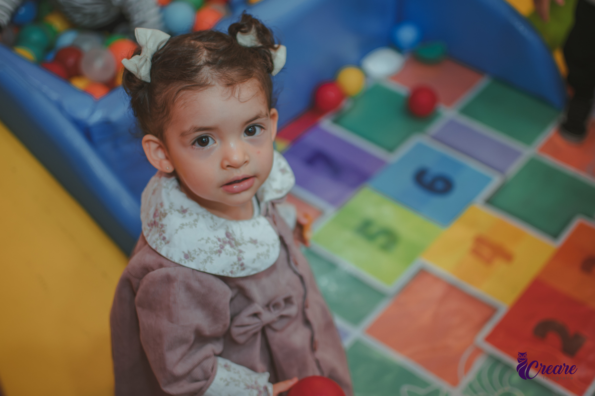 Uma criança olhando para cima, em frente uma piscina de bolinhas durante festa de aniversário infantil.