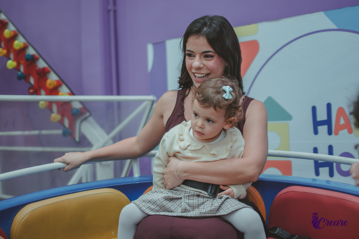 Uma mulher com um criança no colo e varias crianças ao lado, no brinquedo de girar do Buffet Happy House em santo André.