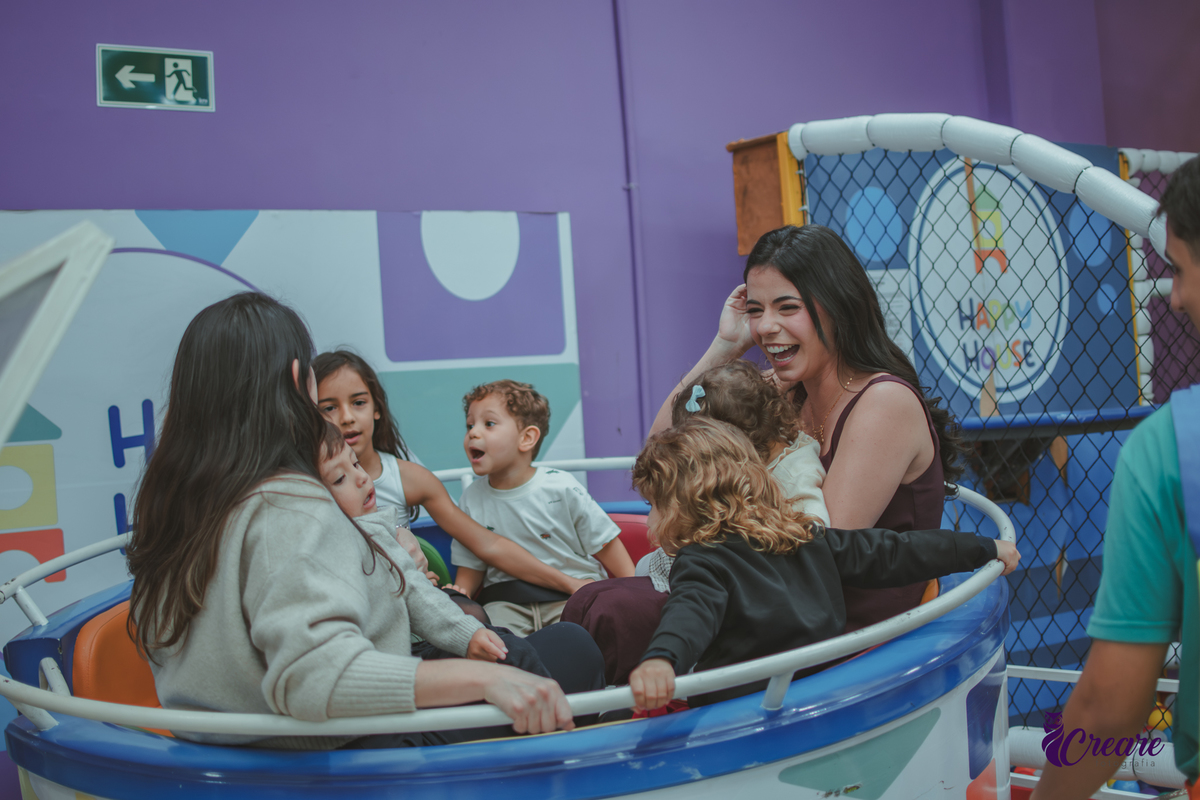 Uma mulher com um criança no colo e varias crianças ao lado, no brinquedo de girar do Buffet Happy House em santo André.