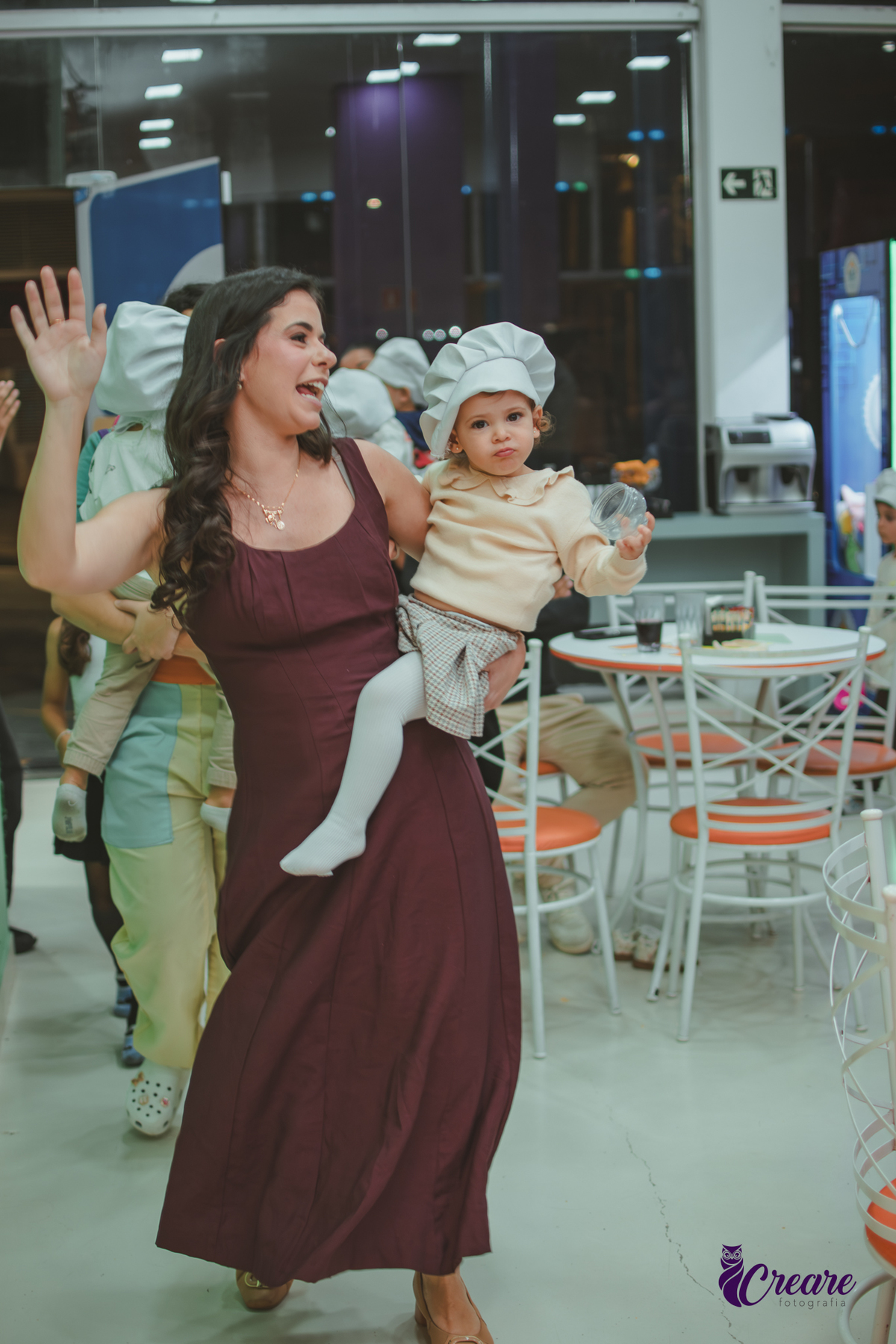 Uma criança de 2 anos usando uma touquinha e sorrindo no colo da sua mãe, durante sua festa de aniversáio no Buffet Happy House em Santo André.