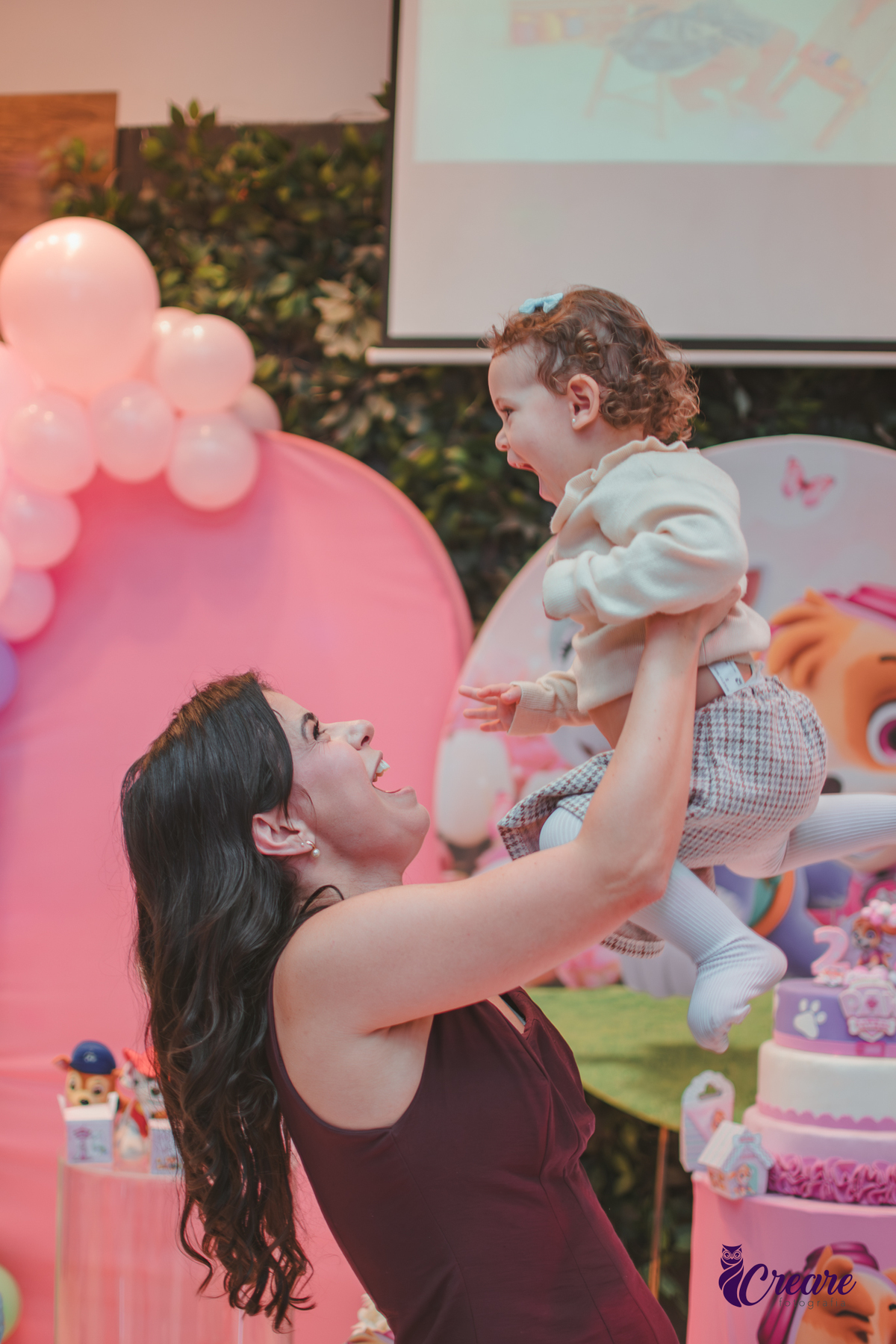 Uma mãe levantando sua filha para o alto em frente a festa de aniversário de 2 anos no buffet Happy House em santo André.