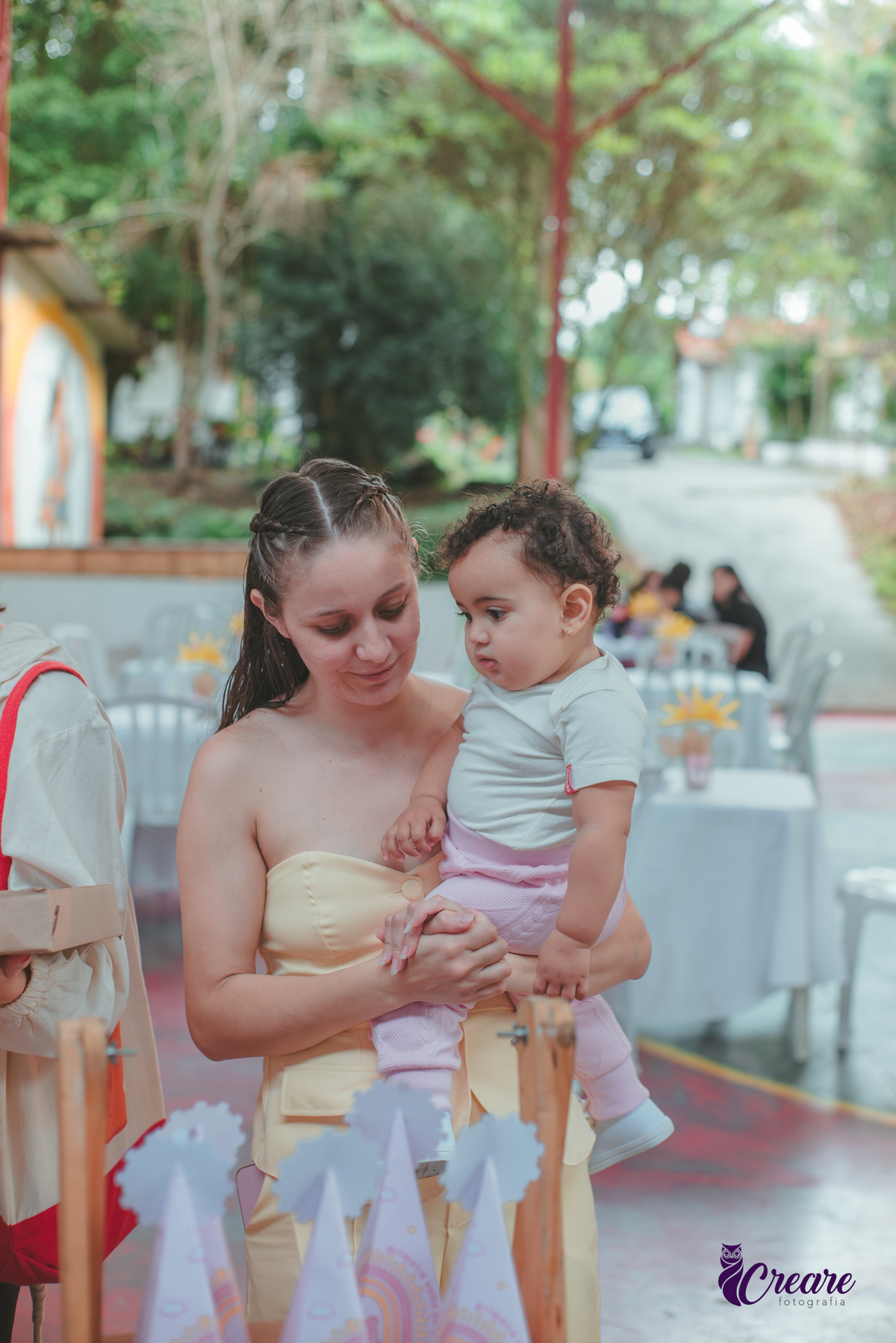 Uma mulher com uma bebê de colo, durante festa de aniversário de 1 ano.