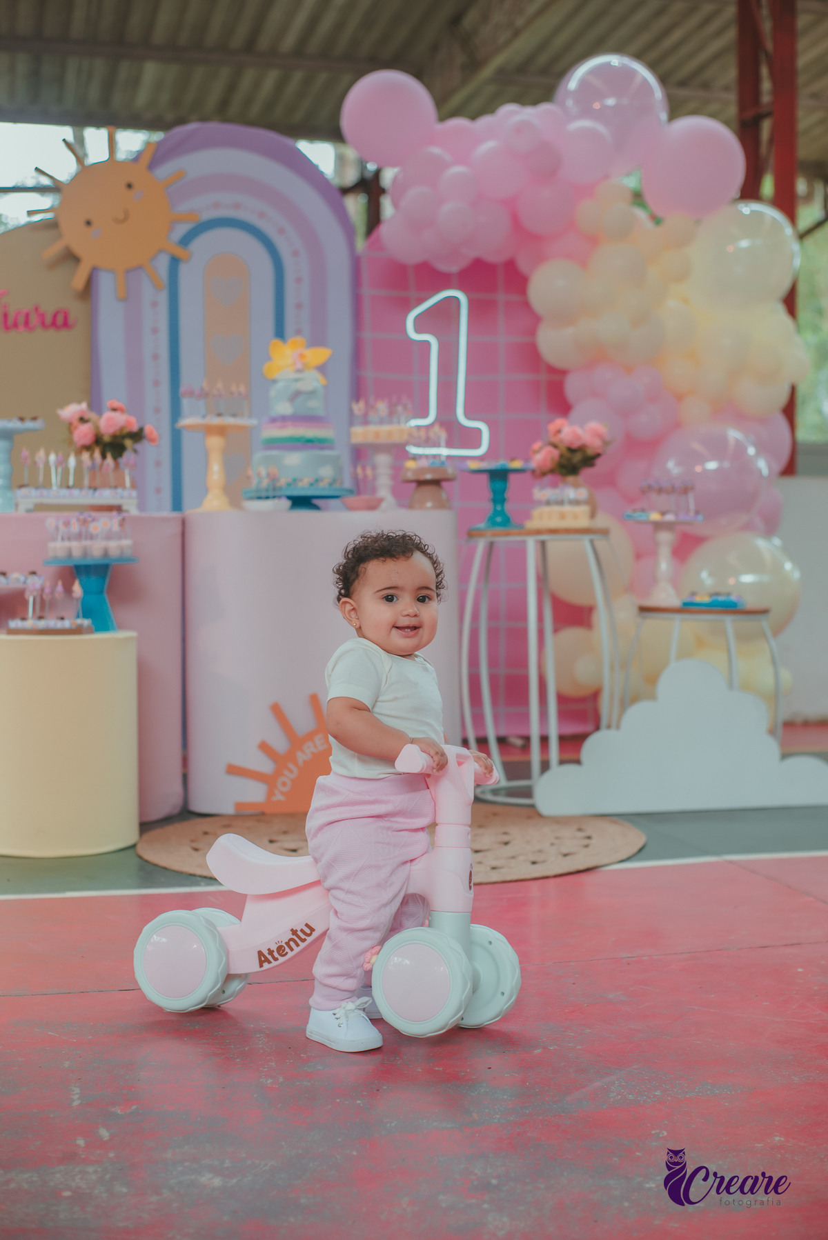 Bebê brincando com um bicicletinha em frente a mesa de decoração do seu aniversáriode 1 ano.