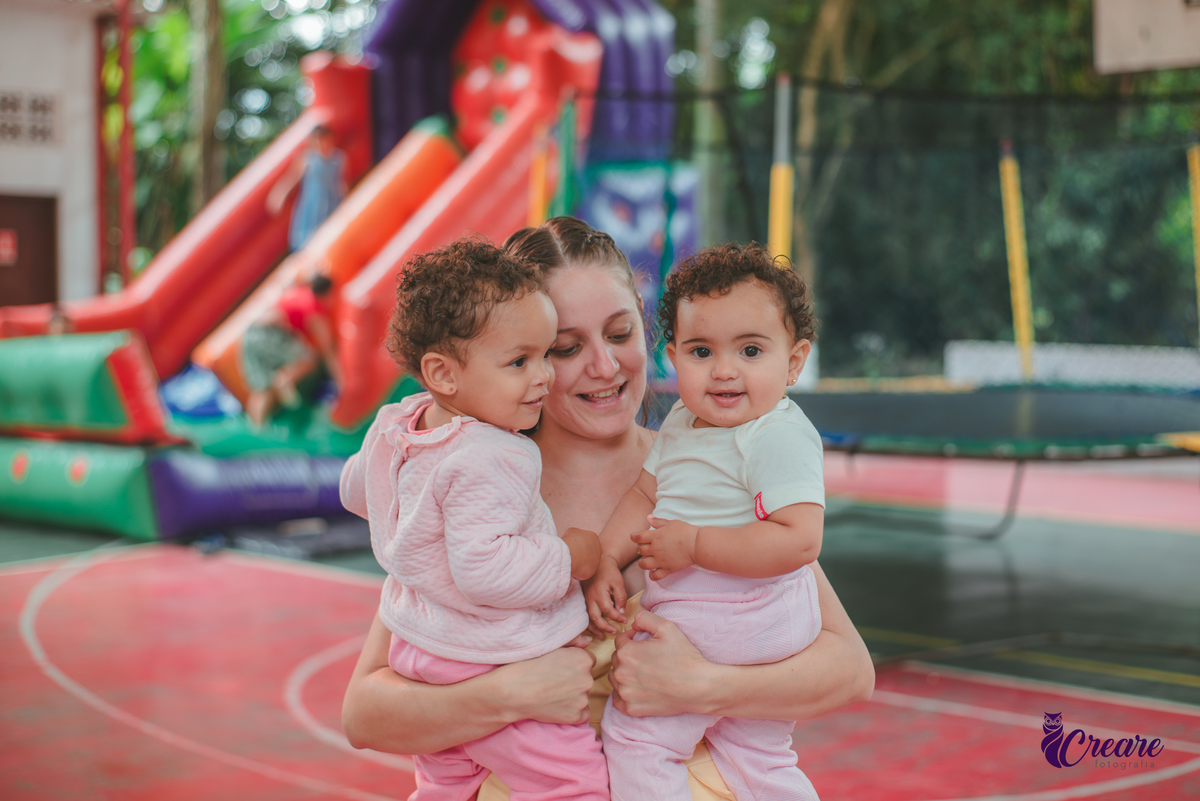 Uma mulher com duas crianças de 1 ano no colo, durante festa de aniversário de 1 ano.