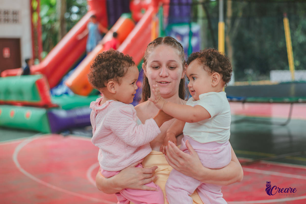 Uma mulher com duas crianças de 1 ano no colo, durante festa de aniversário de 1 ano.