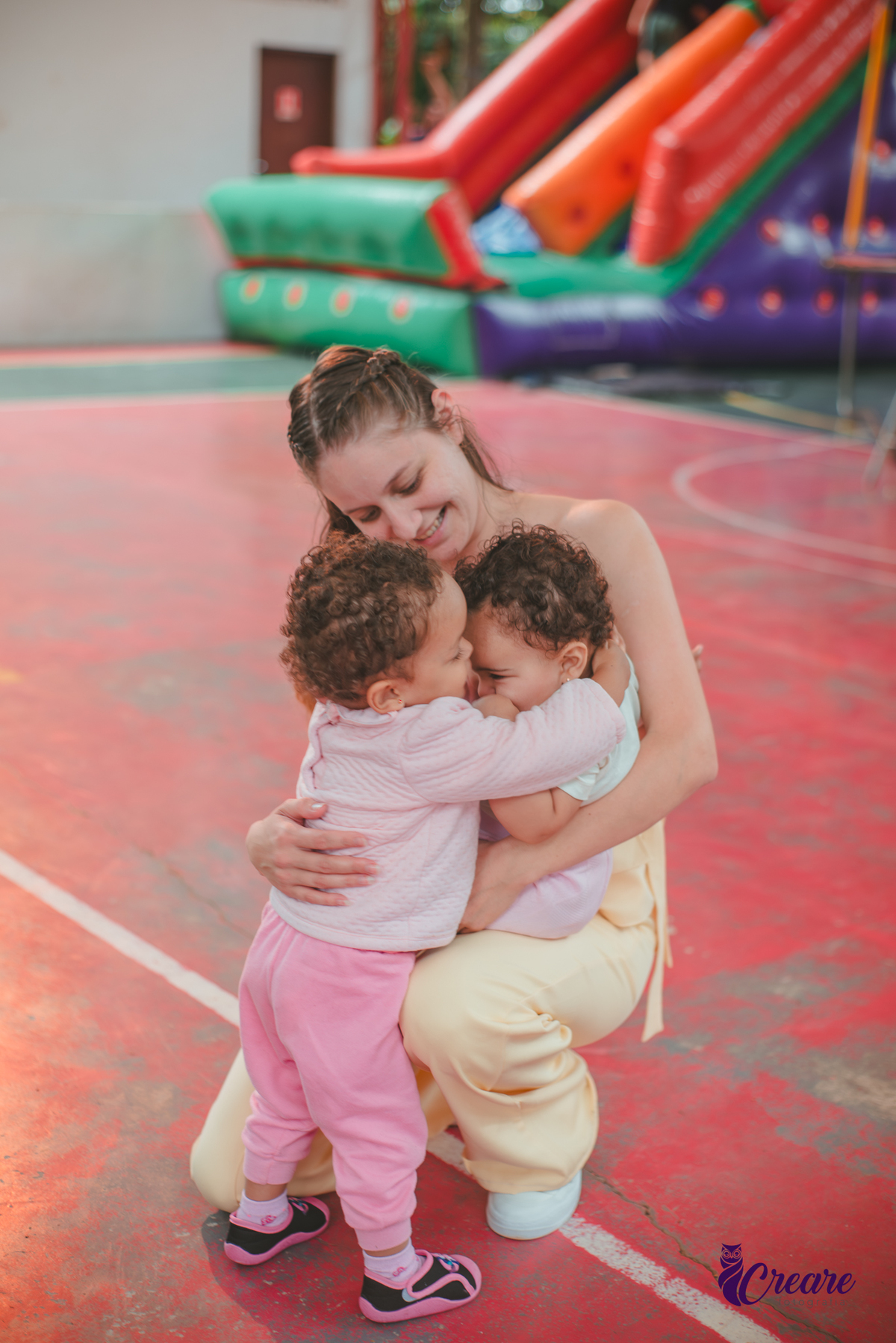 Uma mulher com duas crianças de 1 ano no colo, durante festa de aniversário de 1 ano.