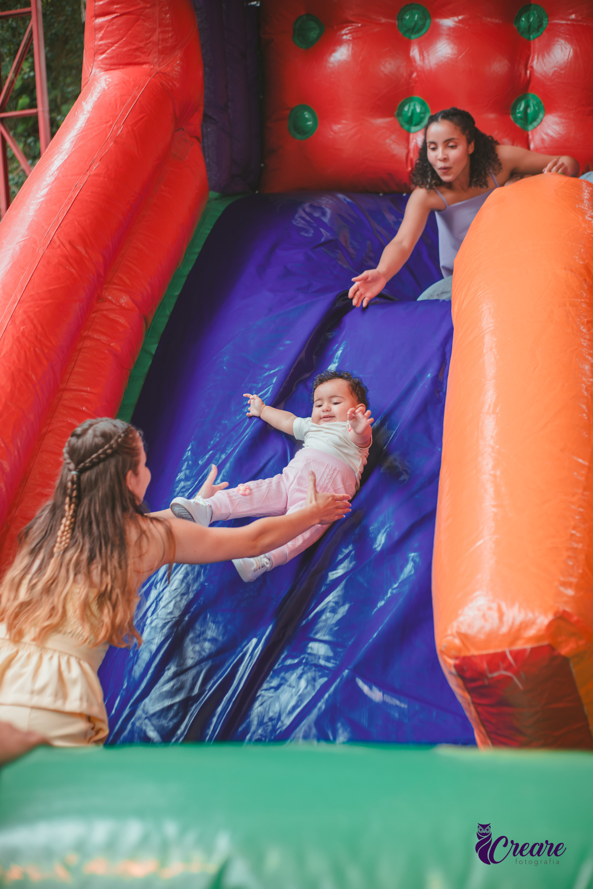 Uma mulher brincando no escorregador de ar, com sua bebê de 1 ano, durante festa de aniversário.