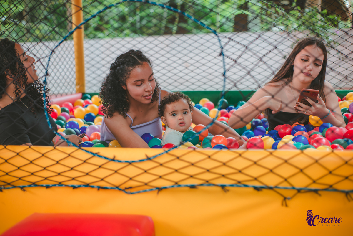 Uma bebê brincando na piscina de bolinhas com outras crianças, durante sua festa de aniversário de 1 ano.