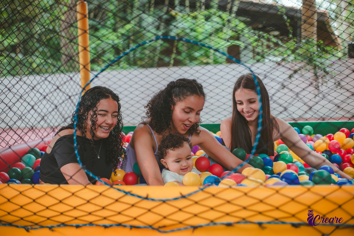 Uma bebê brincando na piscina de bolinhas com outras crianças, durante sua festa de aniversário de 1 ano.