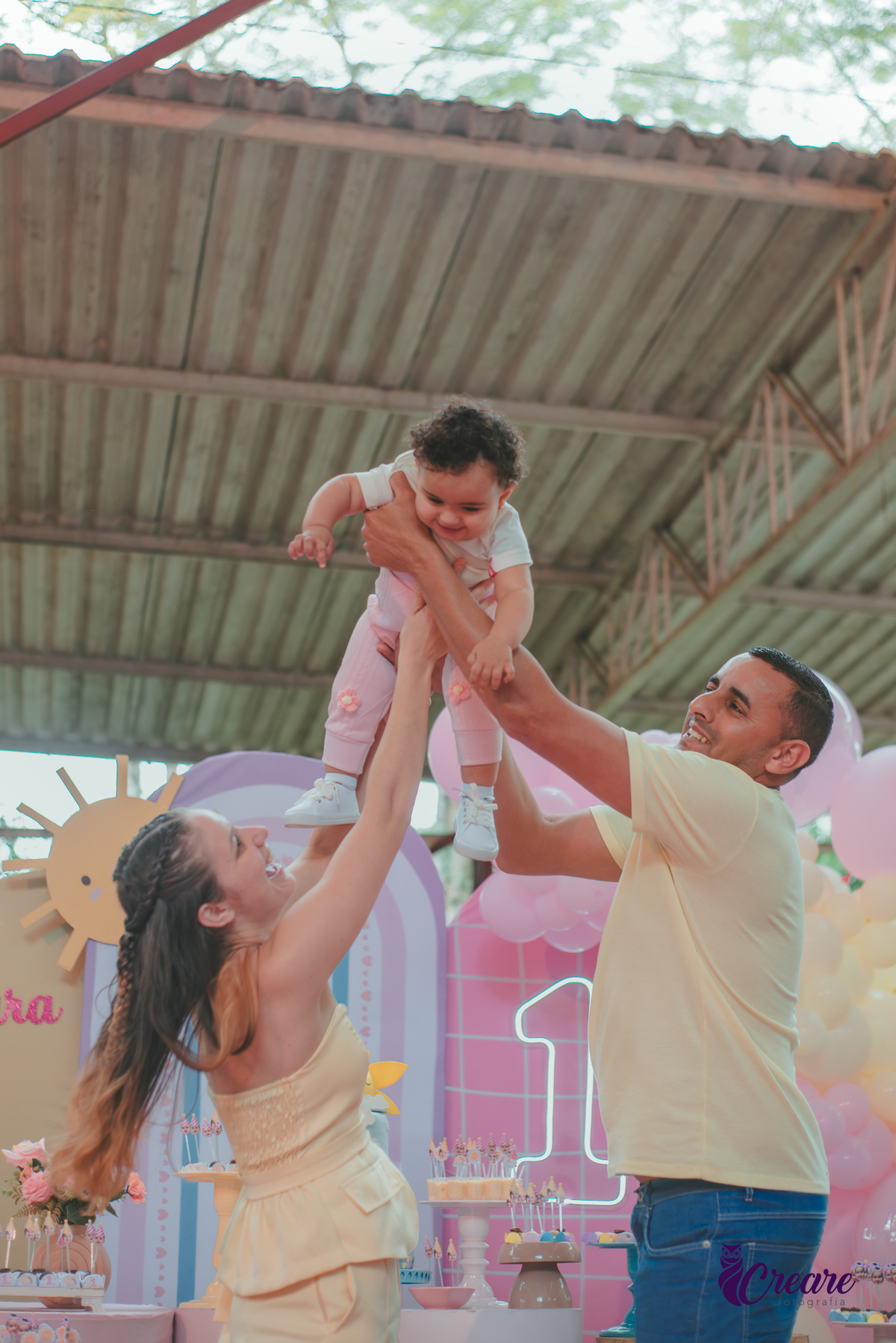 Um casal usando roupa amarela e brincando com um bebêdurante festa de aniversário de 1 ano.