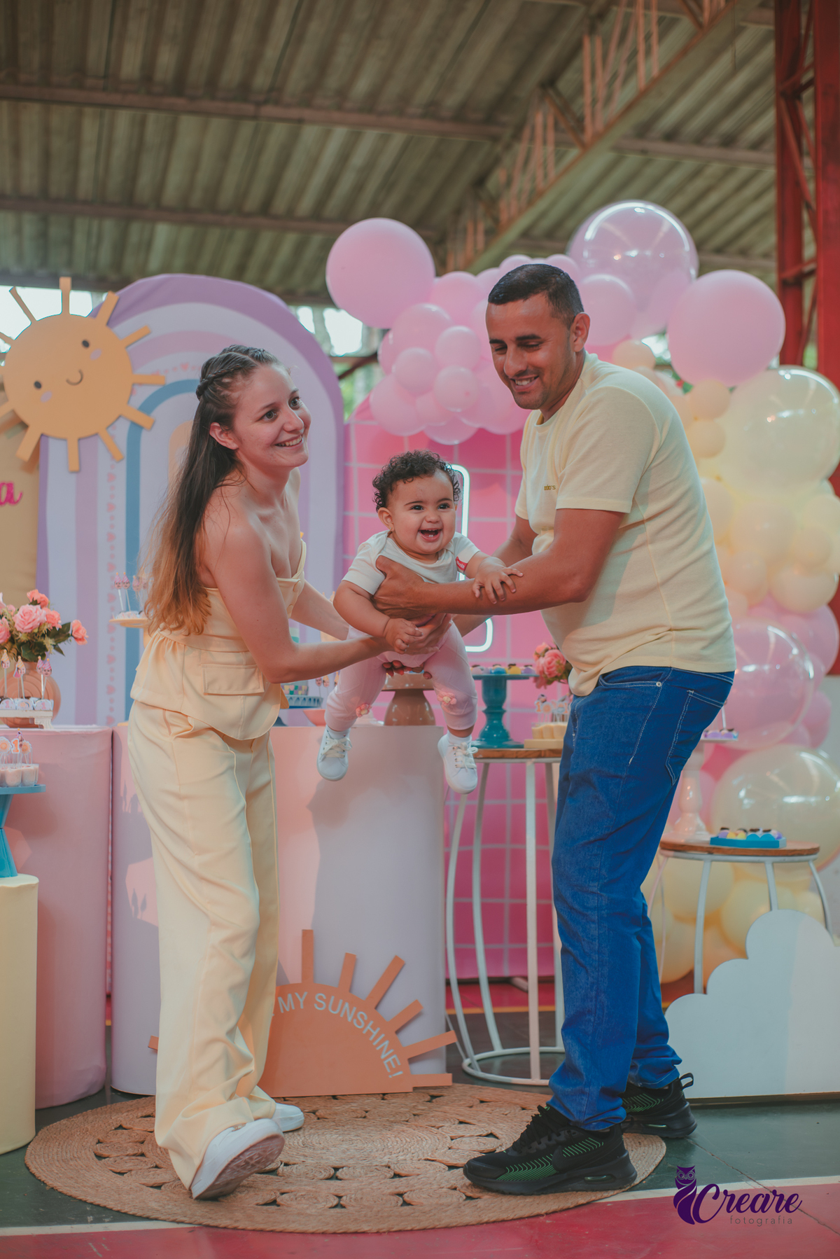 Um casal usando roupa amarela e brincando com um bebêdurante festa de aniversário de 1 ano.
