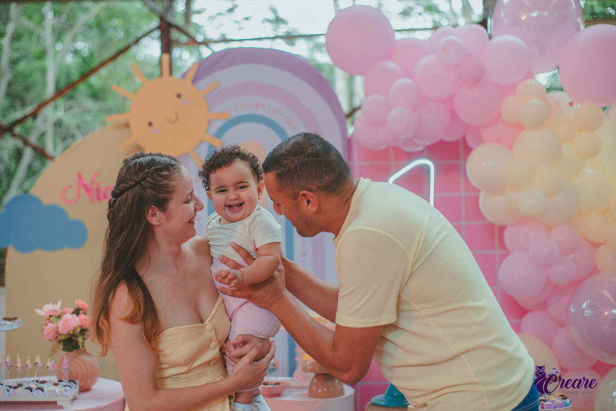 Um casal usando roupa amarela e brincando com um bebêdurante festa de aniversário de 1 ano.