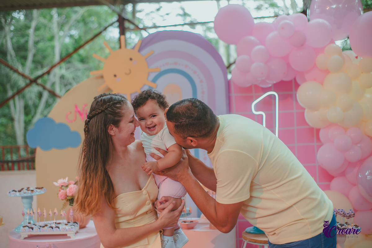 Um casal usando roupa amarela e brincando com um bebêdurante festa de aniversário de 1 ano.