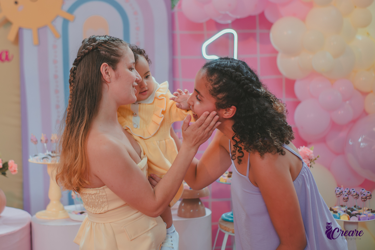 Duas mulheres interagindo com uma bebê durante sua festa de aniversário de 1 ano.