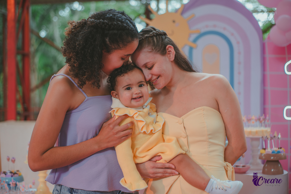 Duas mulheres interagindo com uma bebê durante sua festa de aniversário de 1 ano.