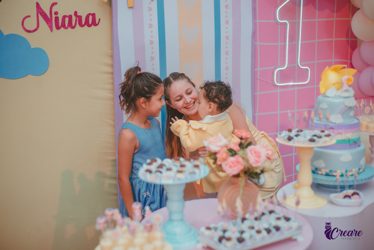 Uma mulhere e uma criança, interagindo com uma bebê durante sua festa de aniversário de 1 ano.