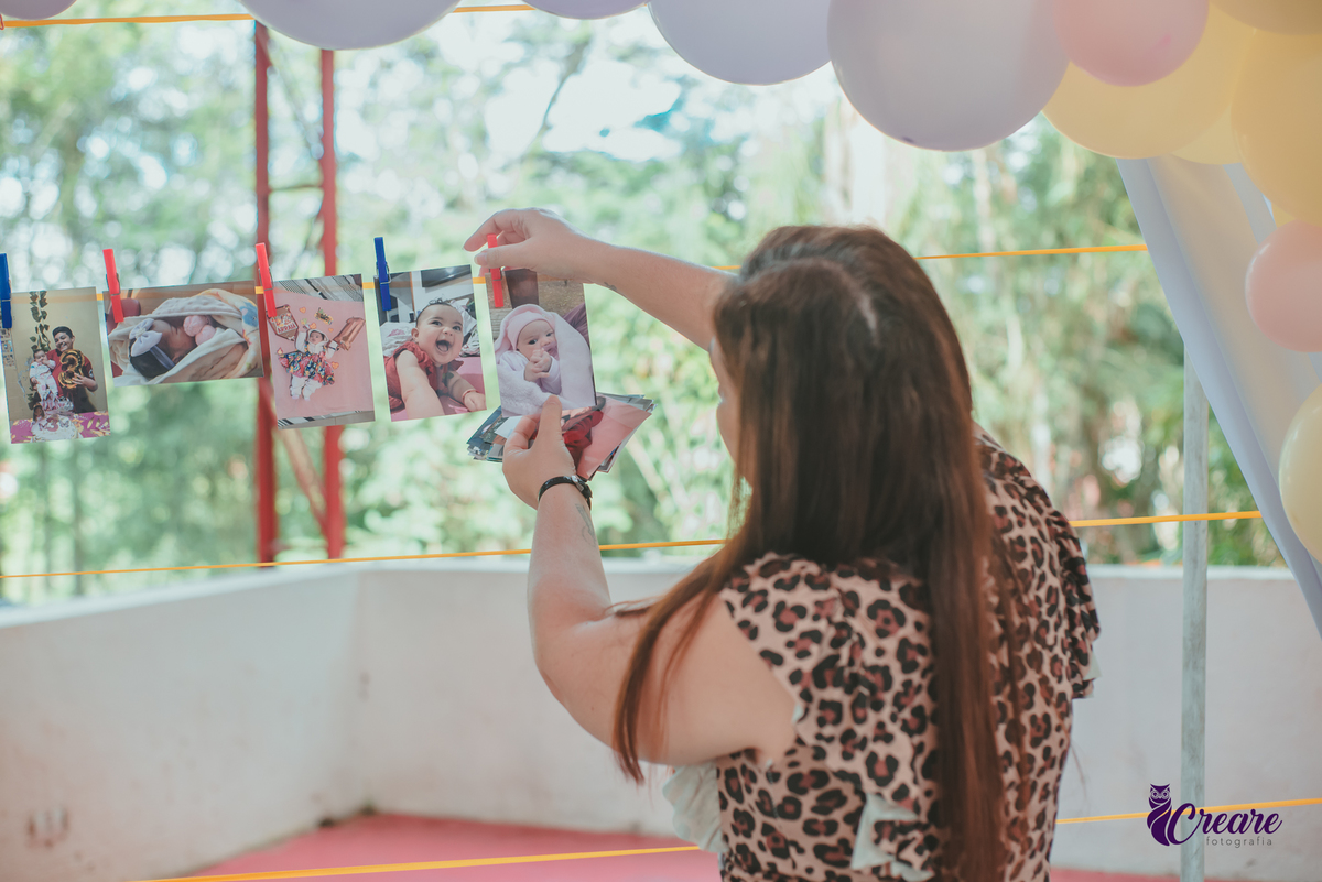 Uma mulher colcando fotos em um varal, para decorar o aniversário de 1 ano de uma criança.