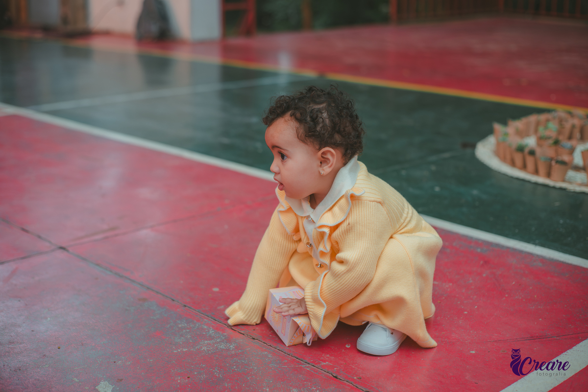 Uma bebê usando vestido amarelo brincando em sua festa de aniversário de 1 ano.