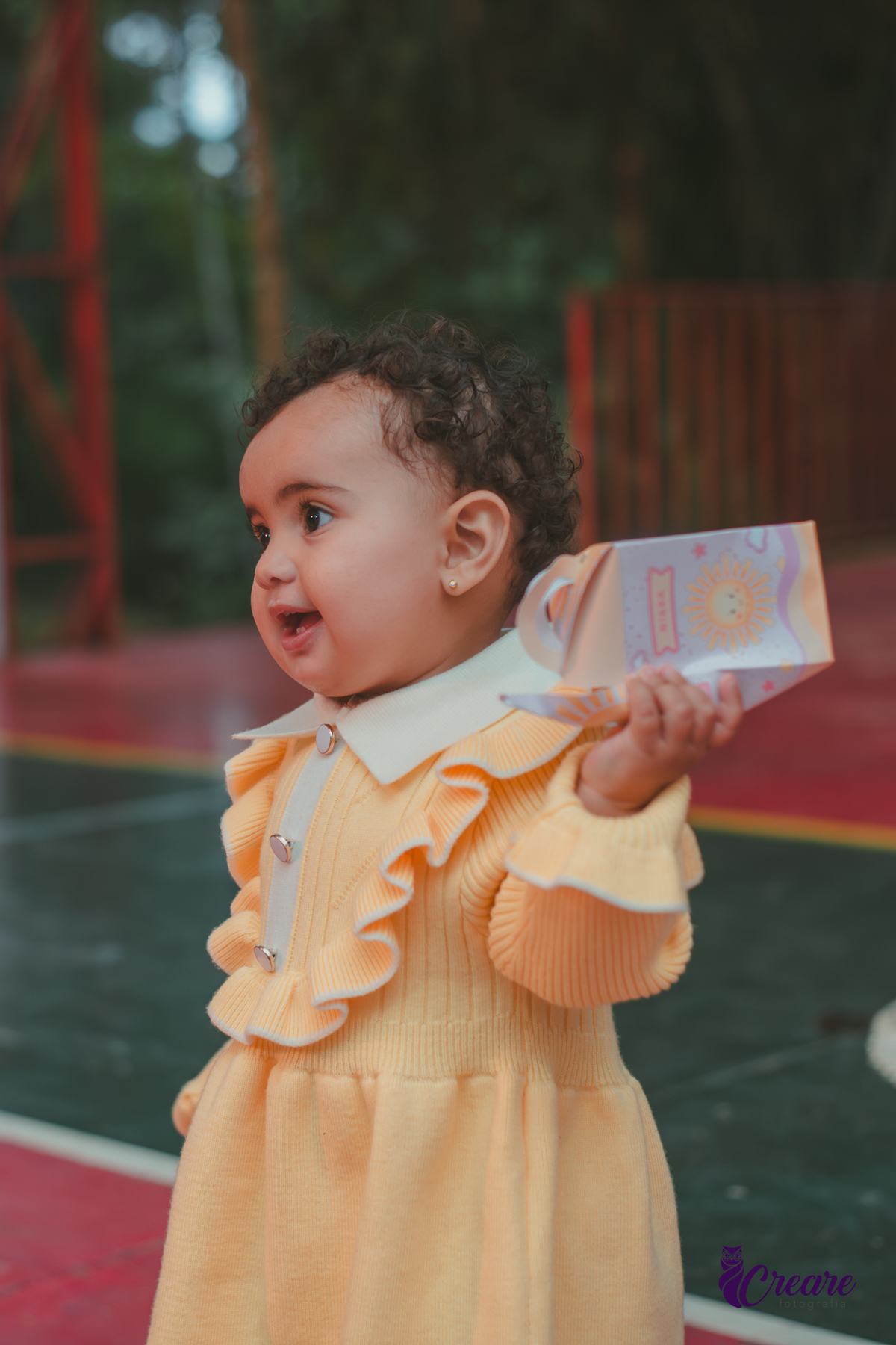 Uma bebê usando vestido amarelo brincando em sua festa de aniversário de 1 ano.