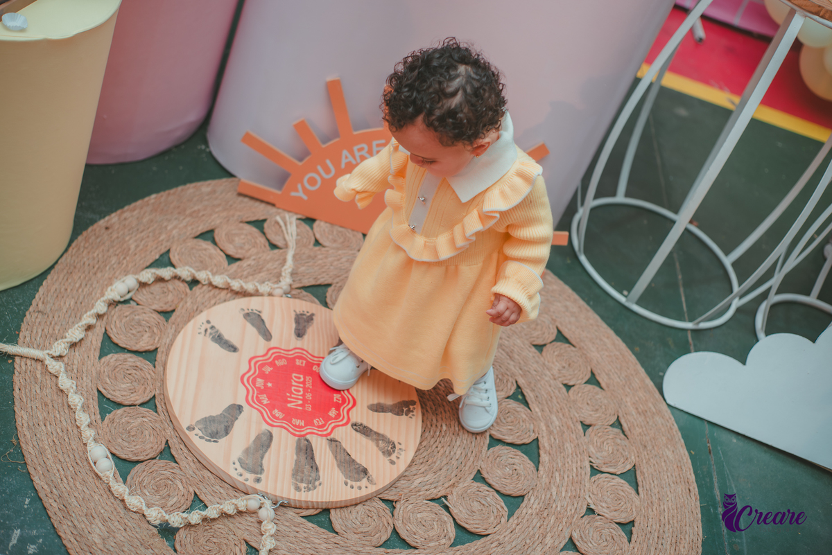 Uma bebê usando vestido amarelo brincando em sua festa de aniversário de 1 ano.