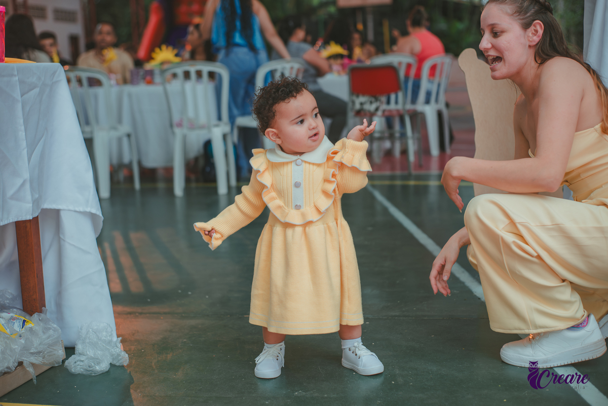 Uma bebê usando vestido amarelo brincando em sua festa de aniversário de 1 ano.