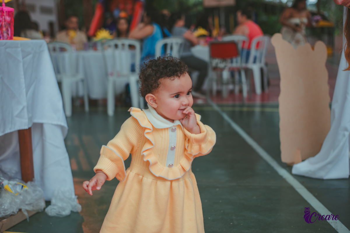 Uma bebê usando vestido amarelo brincando em sua festa de aniversário de 1 ano.