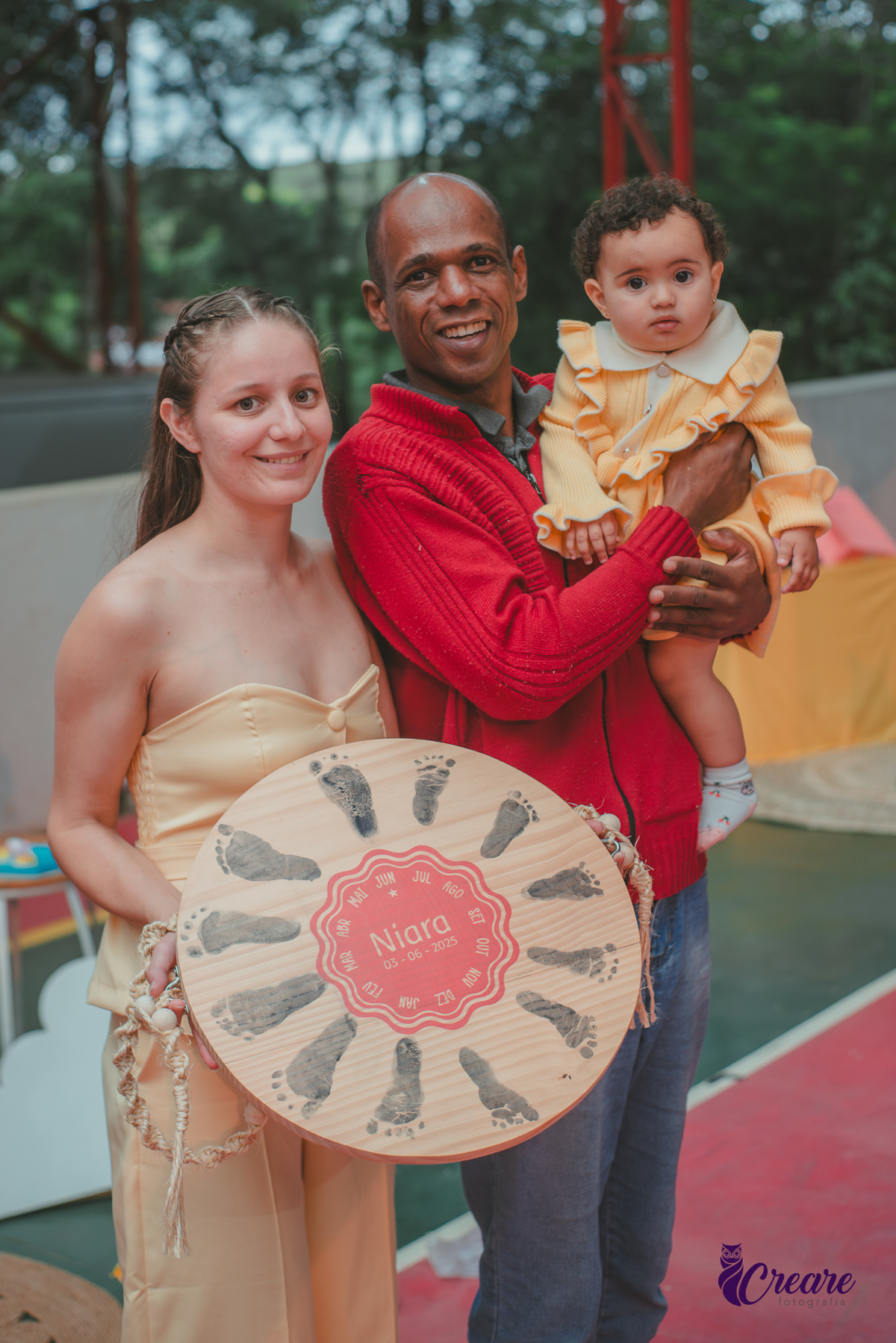 Uma mulher e um homem, segurando a placa de MDF com o carimbo dos pézinhos do bebê, representando a volta ao sol completa.