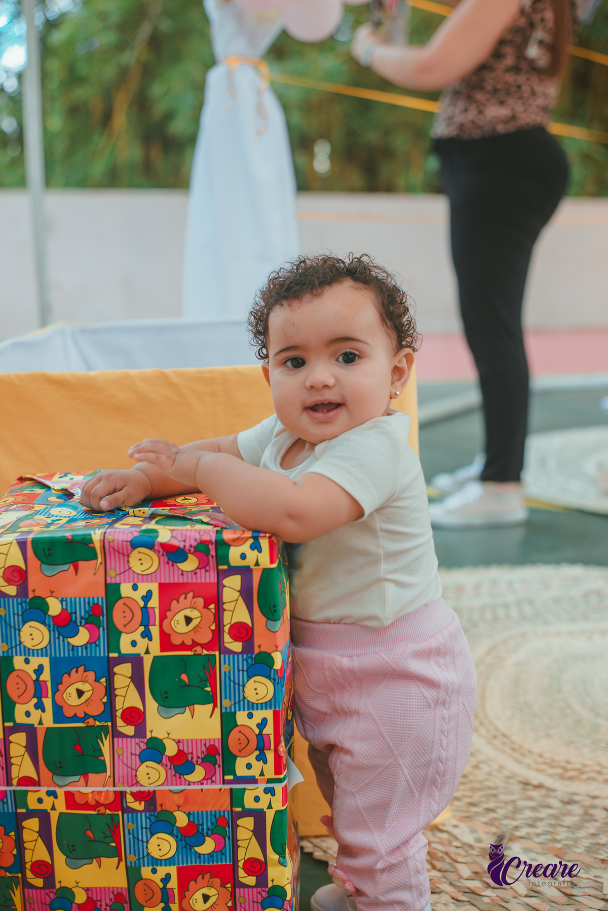 Bebê de um ano sorrindo e brincando com uma caixa de presente, durante sua festa de aniversário.