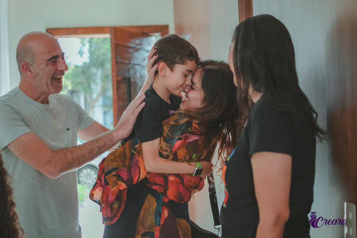 Uma mulher e um homem abraçando uma criança e parabenizando por sua festa de aniversário em casa.