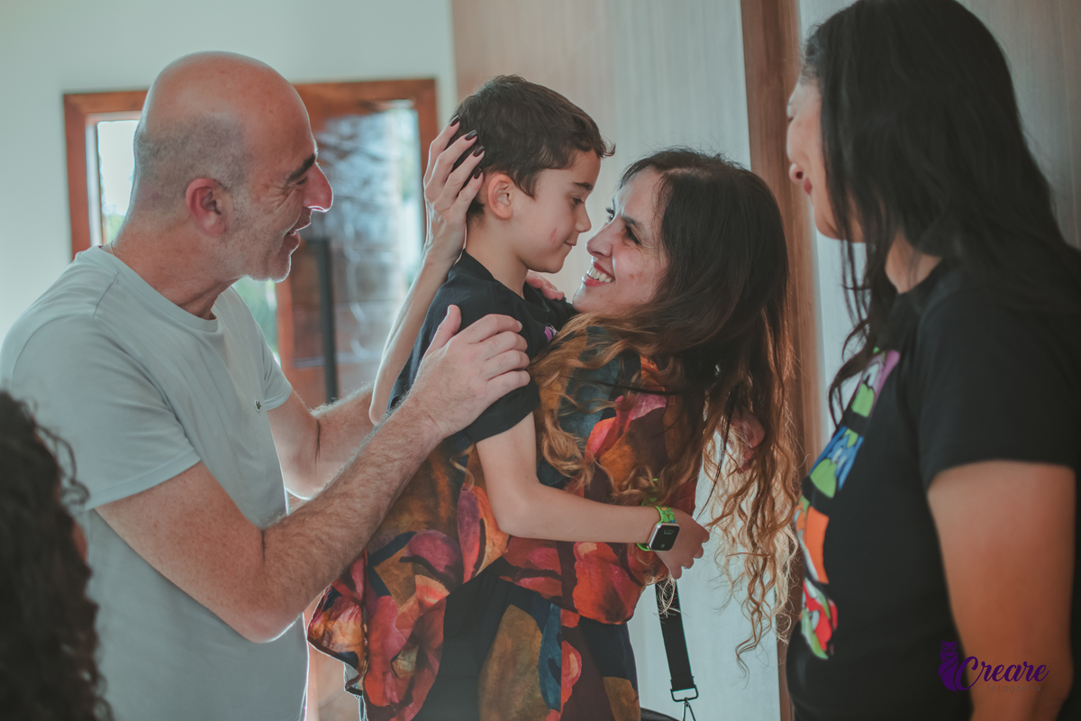 Uma mulher e um homem abraçando uma criança e parabenizando por sua festa de aniversário em casa.