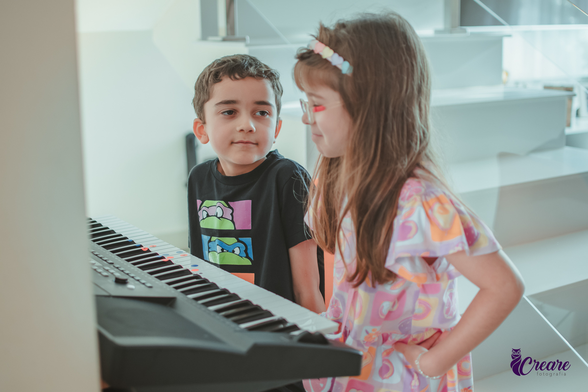 Uma criança ensinando sua amiguinha a tocar teclado durante festa de aniversário em casa.