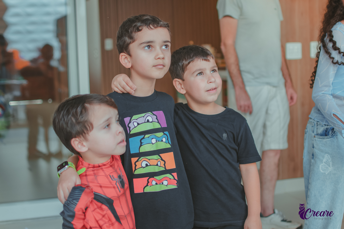 Tres crianças brincando abraçadas, durante festa de aniversário em casa.