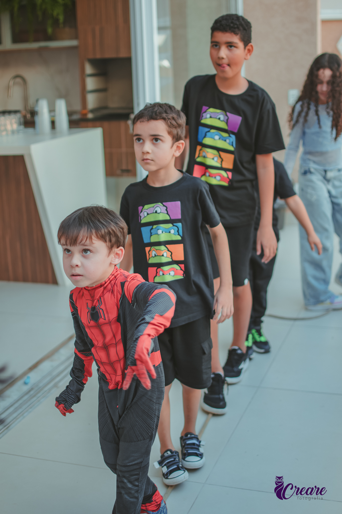 Crianças brincando enfileiradas em uma corda, durante festa de aniversário em casa.