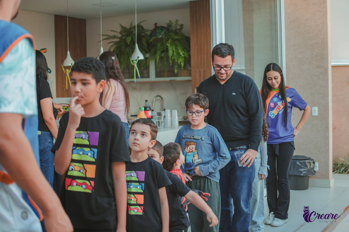 Crianças brincando enfileiradas em uma corda, durante festa de aniversário em casa.