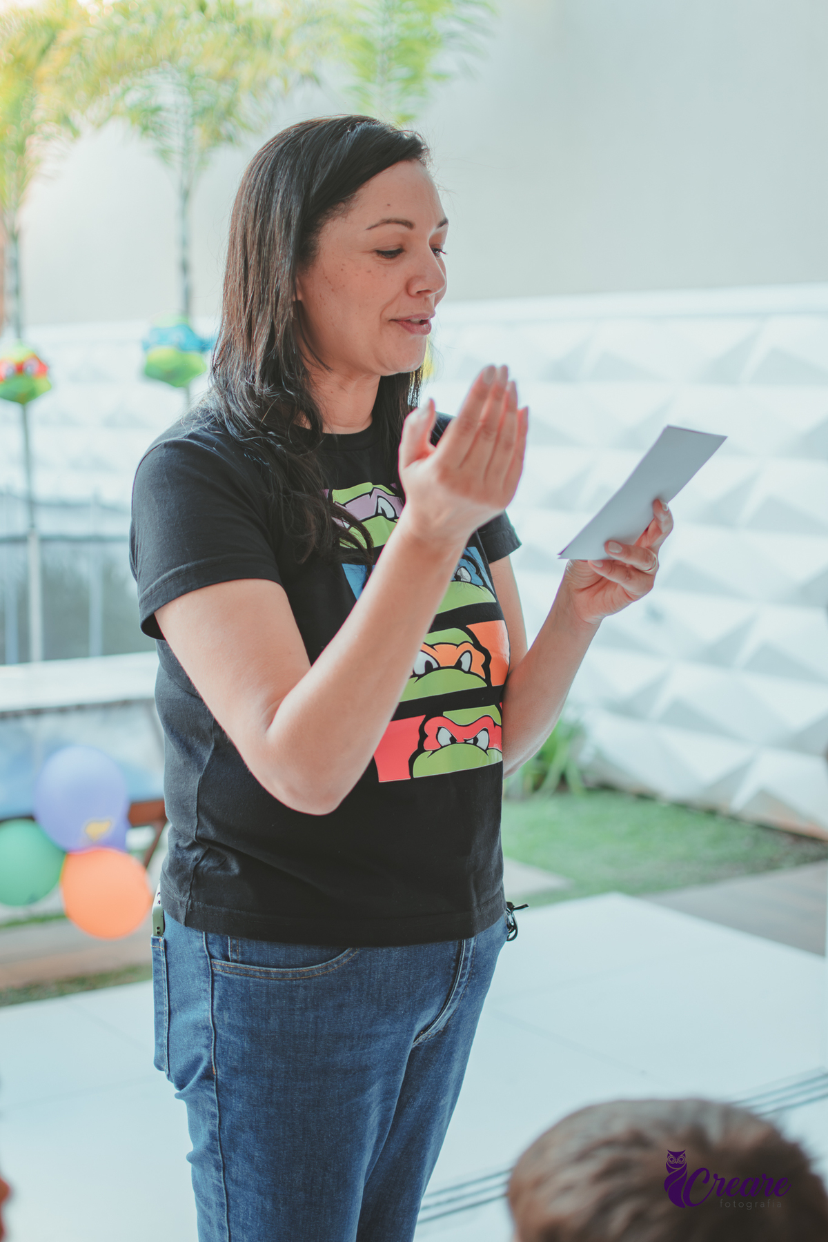 Uma mulher lendo uma brincadeira para crianças, durante festa de aniversário em casa.