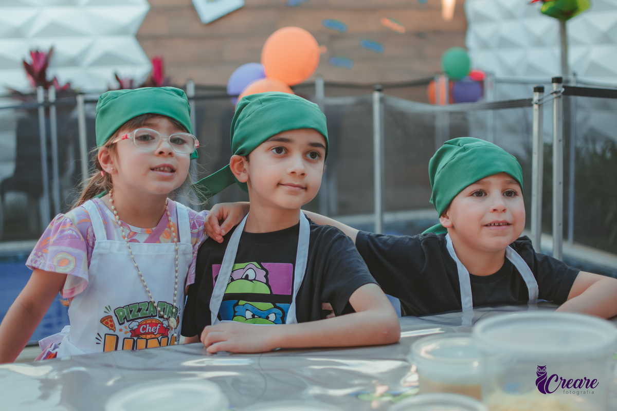 três crianças posando para foto durante festa de aniversário.