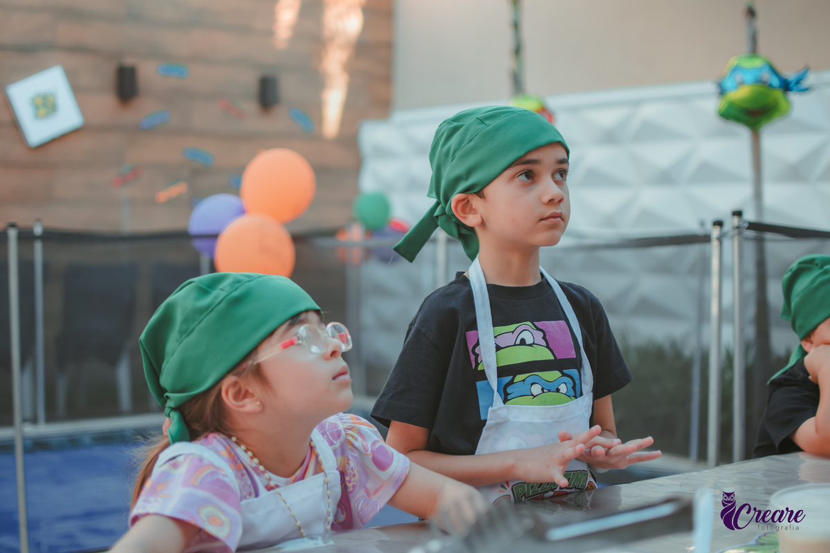 Crianças preparando pizza durante brincadeira de festa de aniversário infantil em casa.