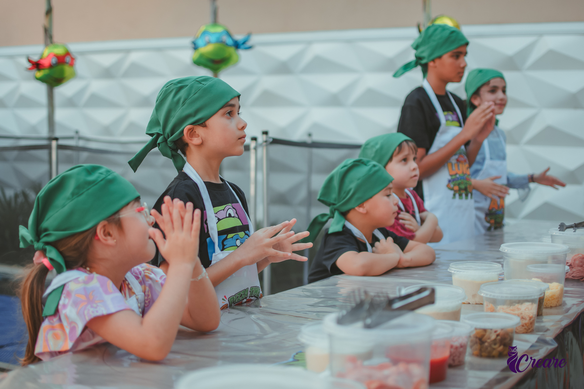 Crianças preparando pizza durante brincadeira de festa de aniversário infantil em casa.