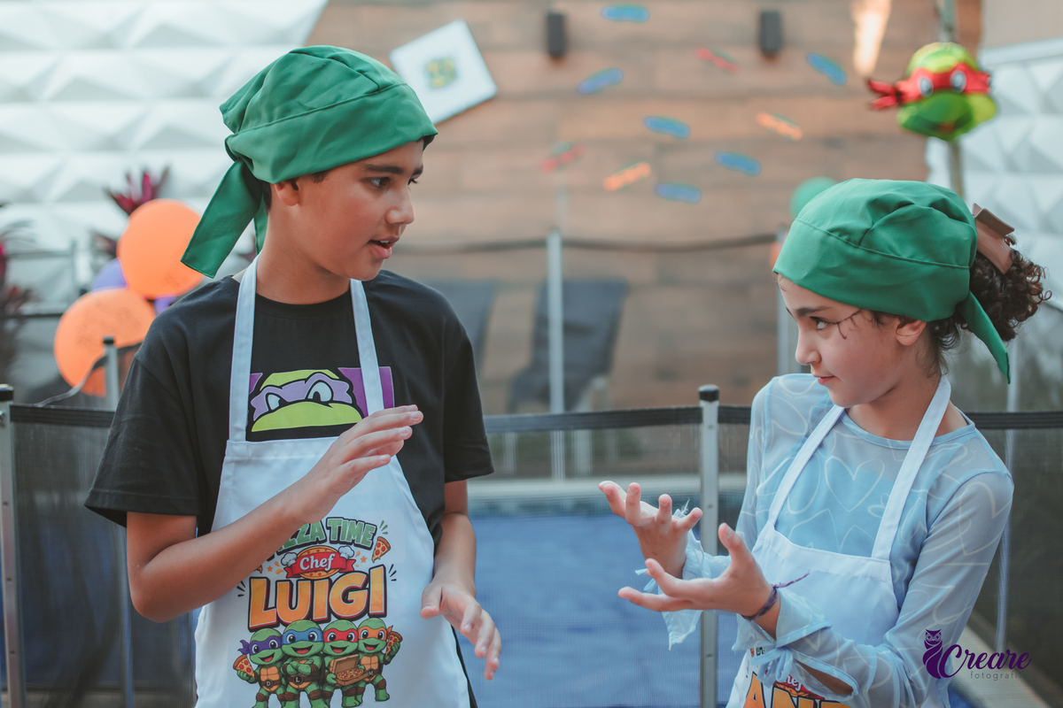 Crianças preparando pizza durante brincadeira de festa de aniversário infantil em casa.