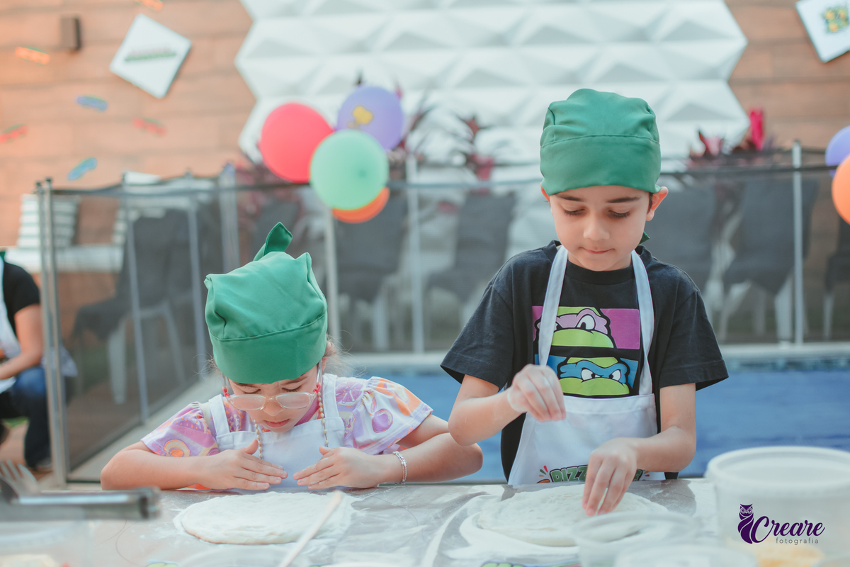 Crianças preparando pizza durante brincadeira de festa de aniversário infantil em casa.