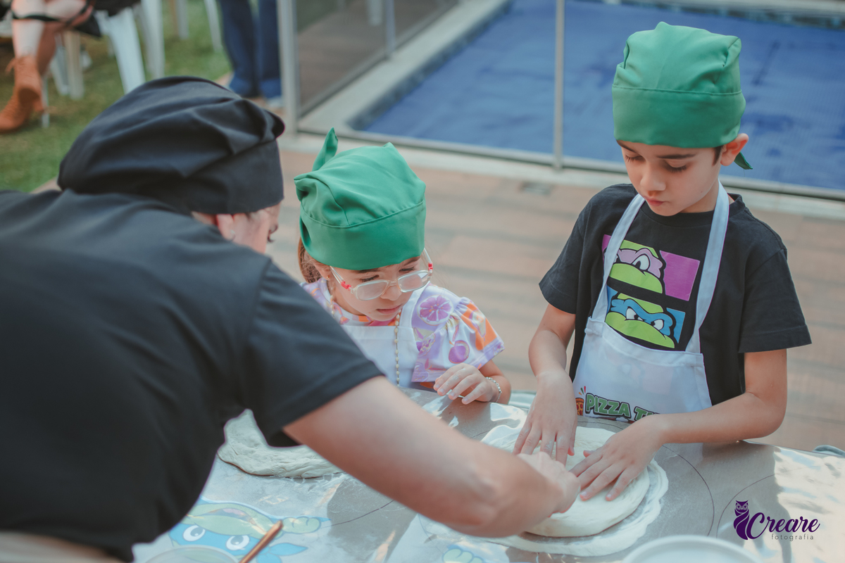 Crianças preparando pizza durante brincadeira de festa de aniversário infantil em casa.