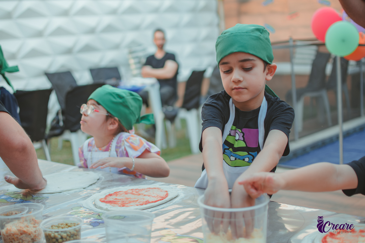 Crianças preparando pizza durante brincadeira de festa de aniversário infantil em casa.