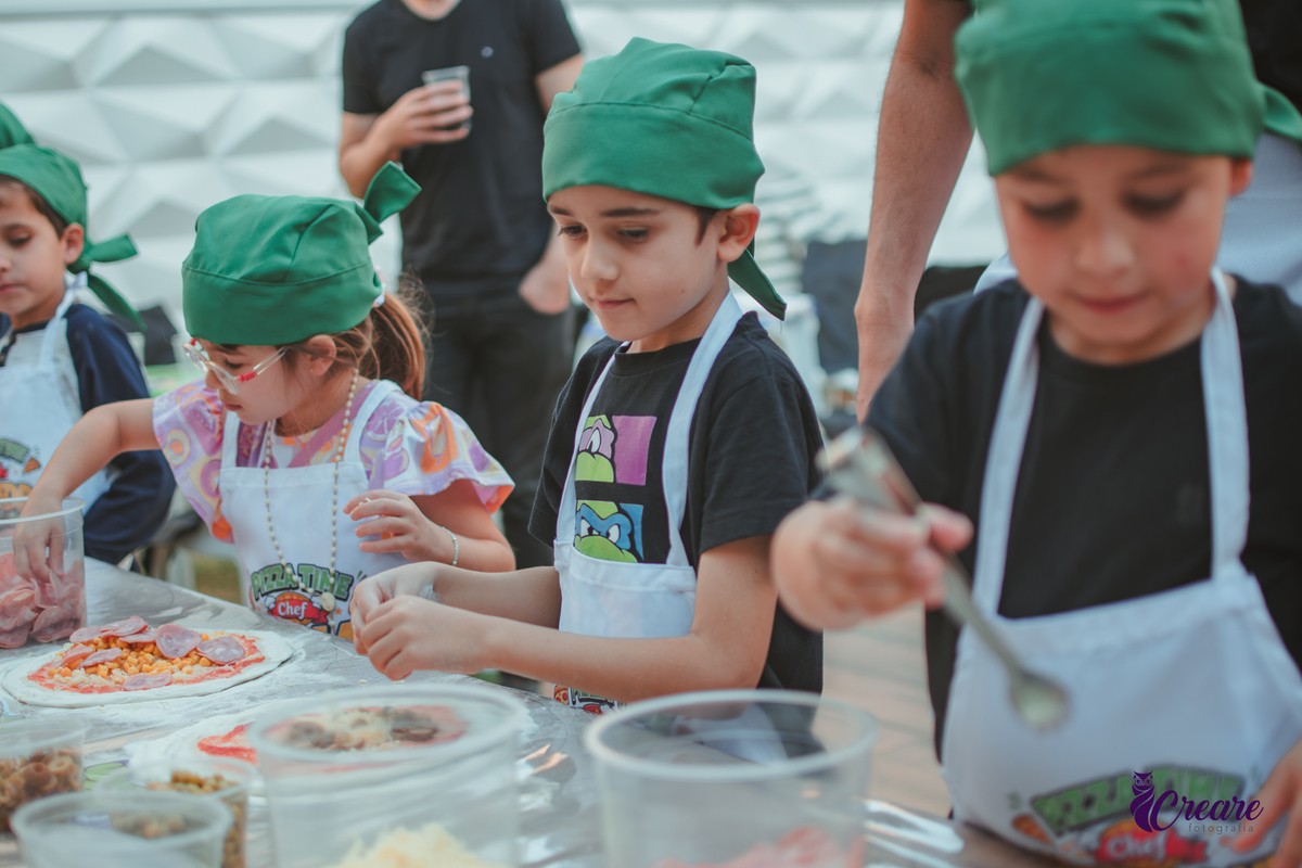 Crianças preparando pizza durante brincadeira de festa de aniversário infantil em casa.