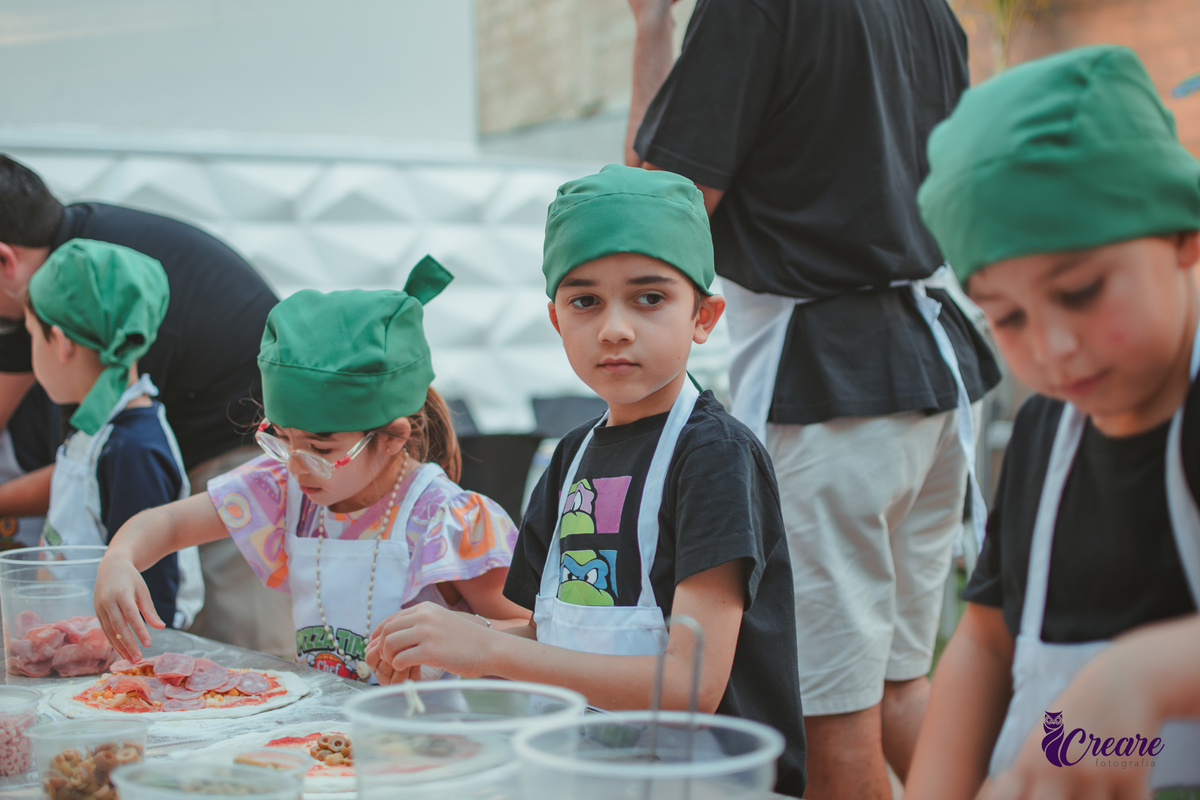 Crianças preparando pizza durante brincadeira de festa de aniversário infantil em casa.