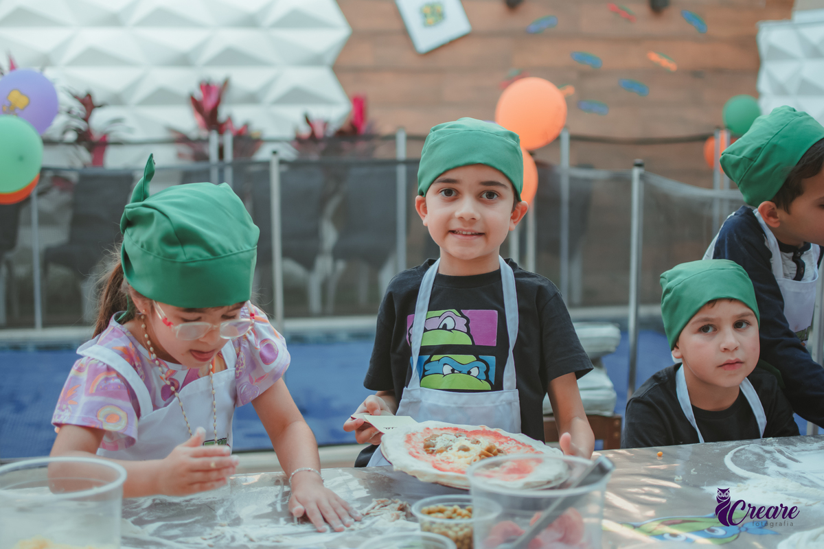 Crianças preparando pizza durante brincadeira de festa de aniversário infantil em casa.